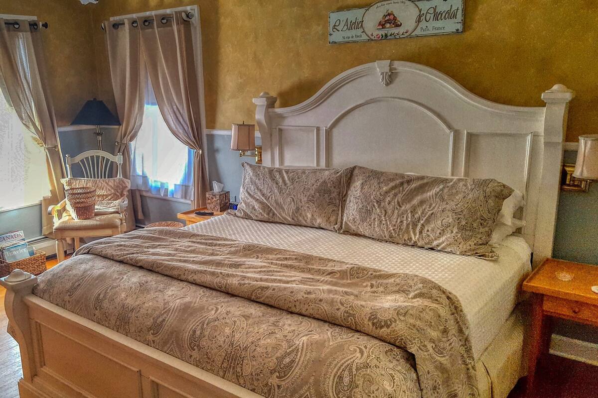 A bedroom with a large bed, a chair, a nightstand, and a wall clock.