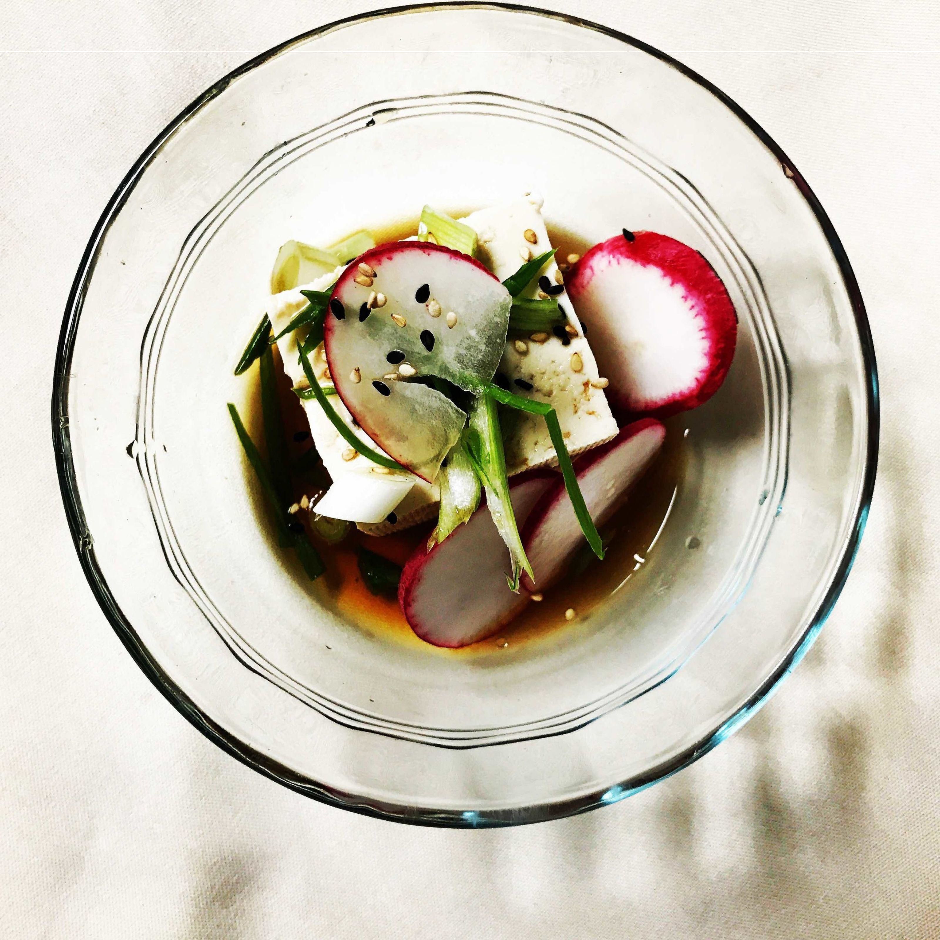 A glass bowl containing a dish with radishes, green onions, and a white sauce.