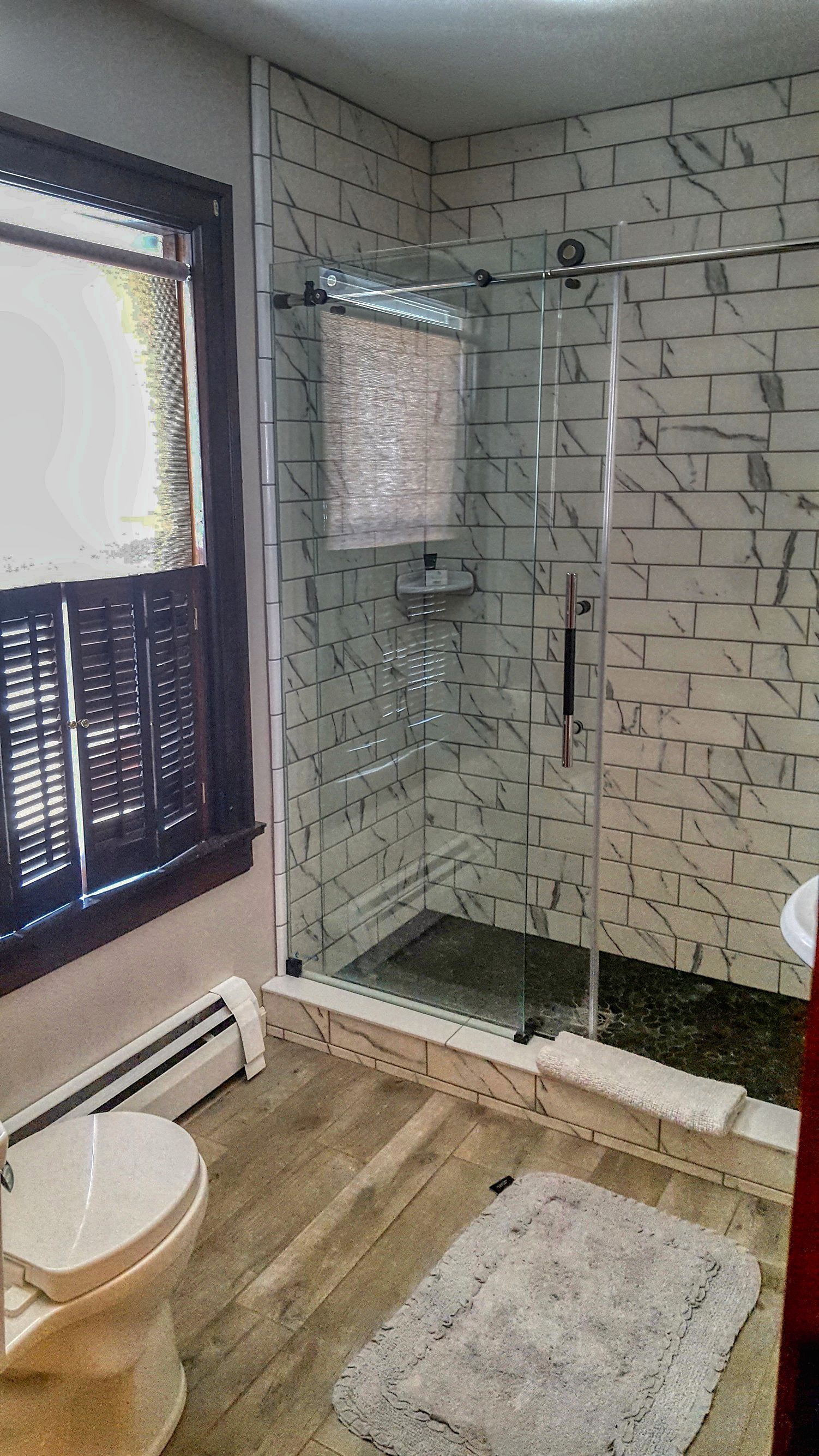 A bathroom with a toilet, a glass shower enclosure, and a window with blinds.