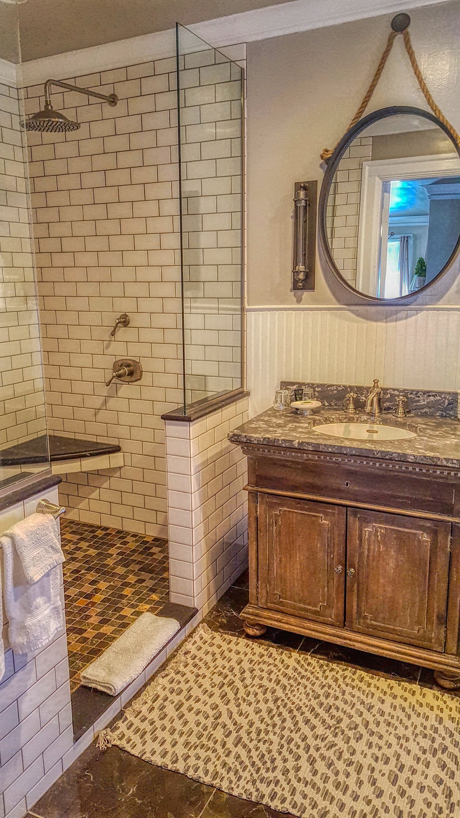 A bathroom with a shower, a vanity with a mirror, and a patterned rug on the floor.
