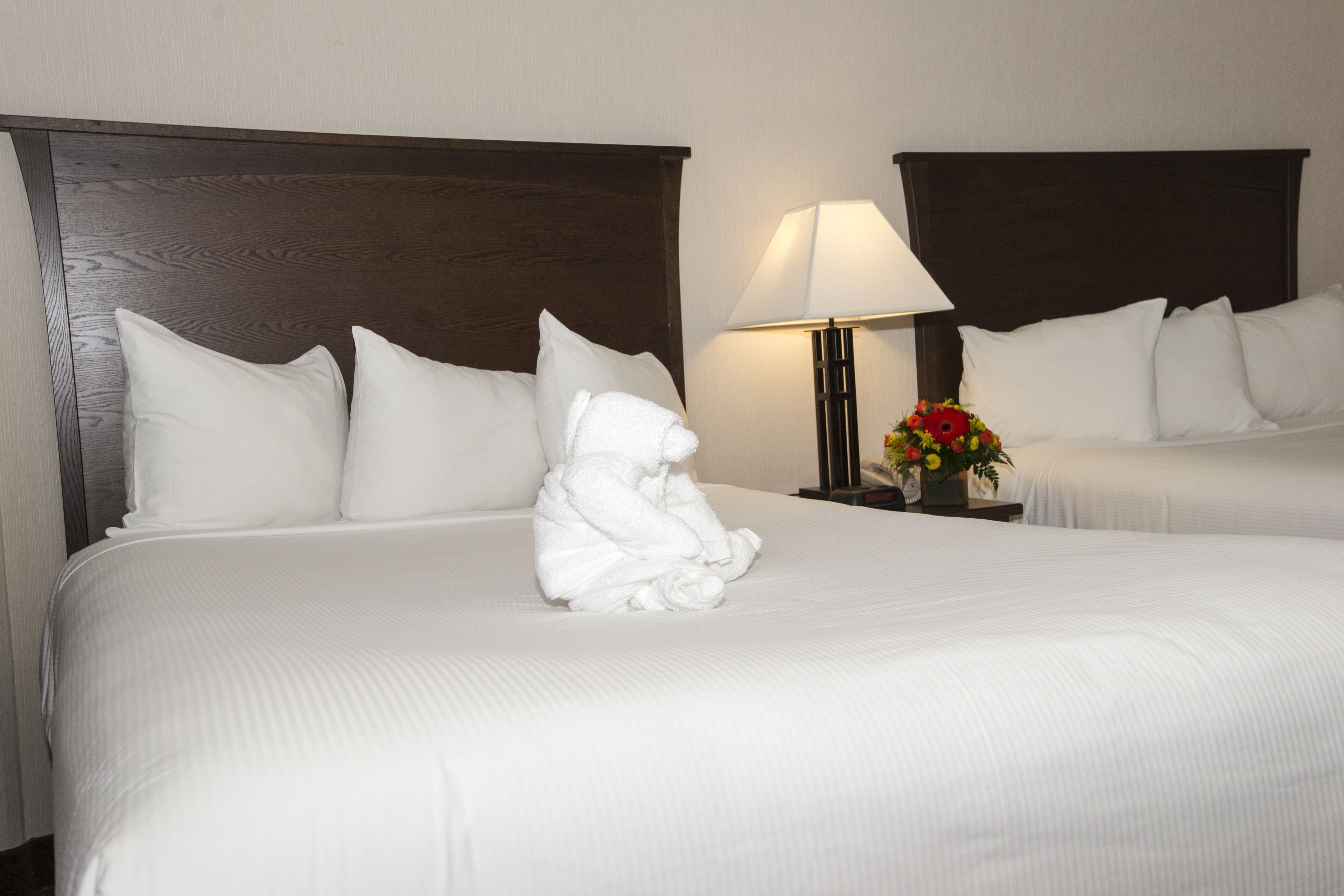 A hotel room with two beds, a nightstand with a lamp, and a floral arrangement.