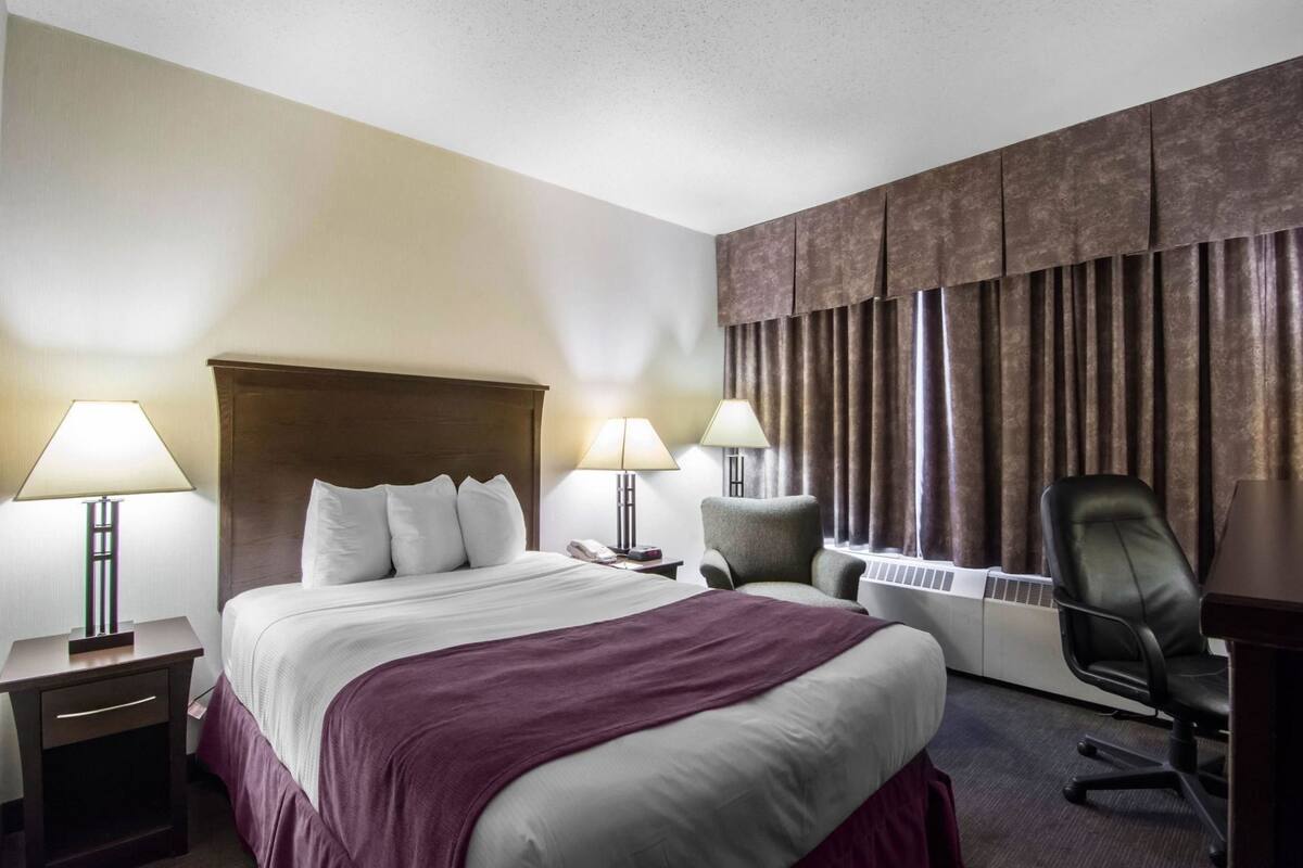 Habitación de hotel con una cama grande, dos lámparas de noche, un escritorio con silla y un amplio ventanal con cortinas.