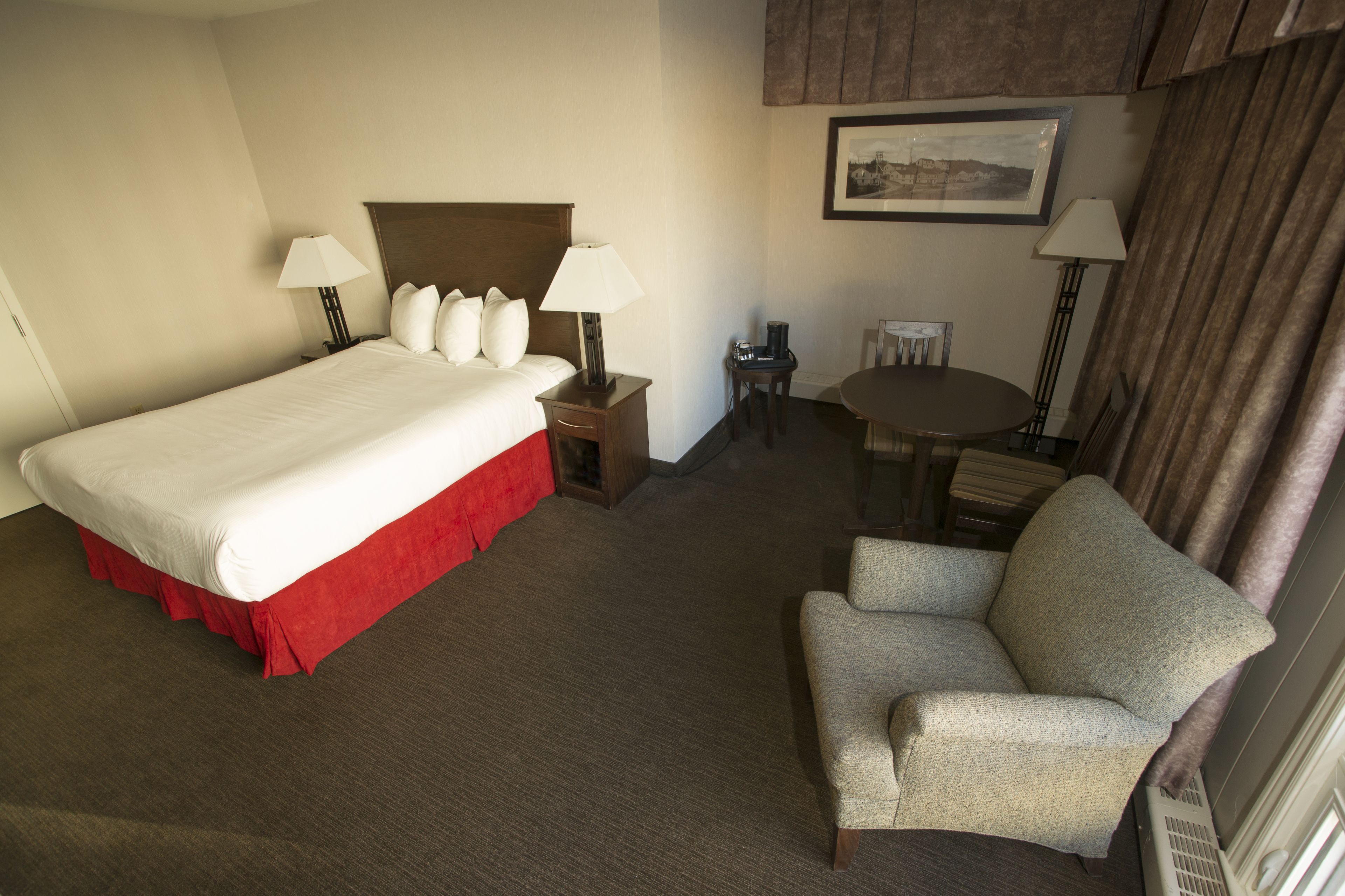 Una camera d'albergo con un letto grande, due comodini con lampade, un tavolino rotondo, una sedia e un quadro appeso al muro.