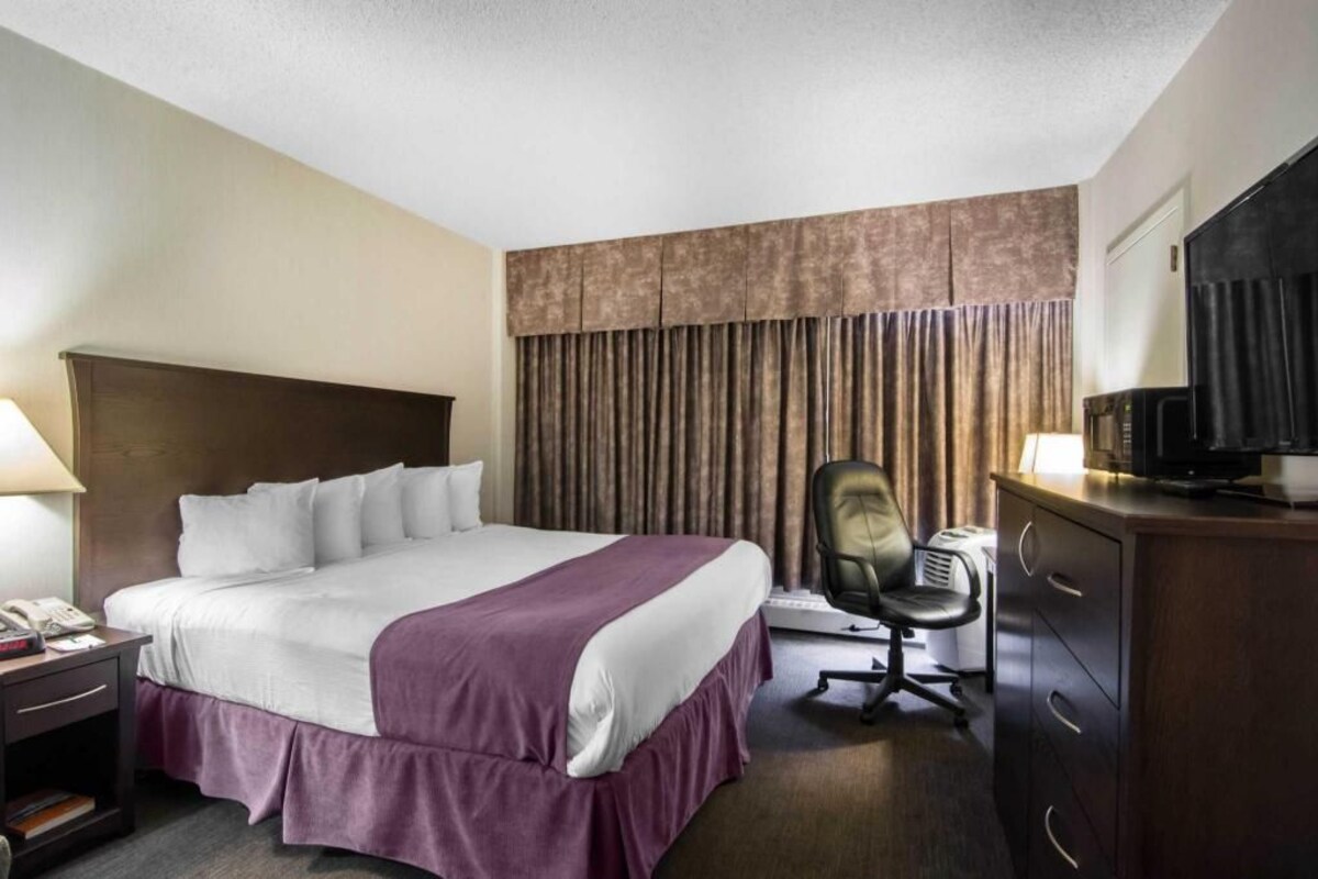 Ein Hotelzimmer mit Bett, Schreibtisch mit Stuhl, Fernseher und einer Minibar.