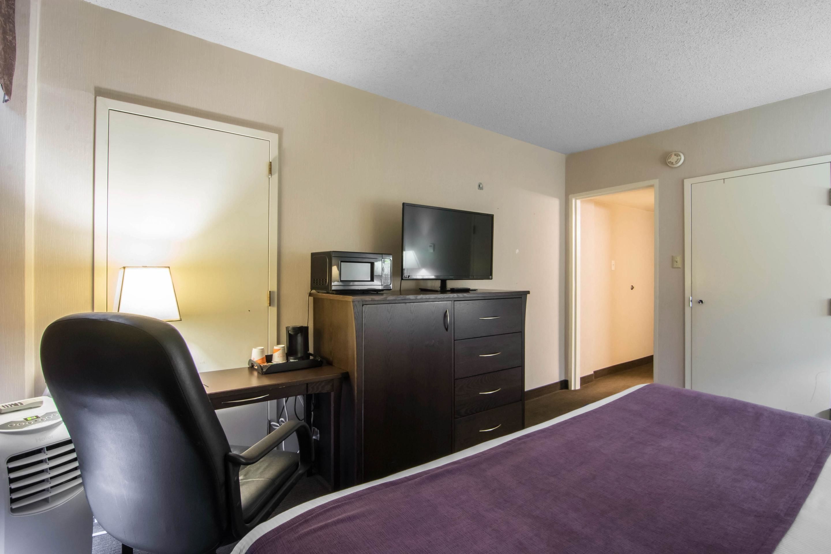 A hotel room with a bed, a desk with a computer, a television, and a dresser.