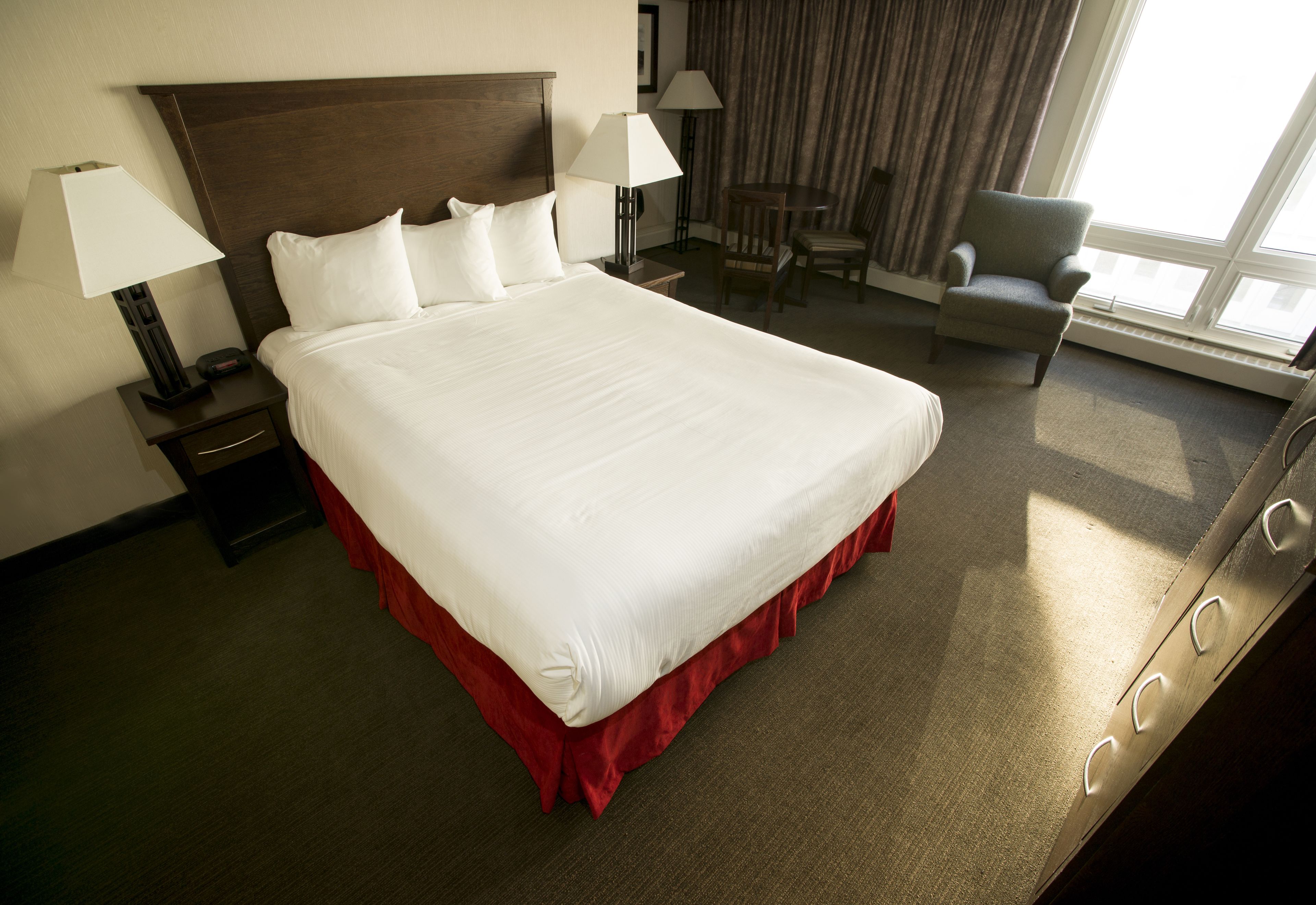 A hotel room with a large bed, two bedside tables with lamps, a chair, and a view of the outdoors through a window.