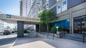 A hotel entrance with a sign reading "Quality Inn & Suites," a staircase leading to the entrance, and a tree in front.