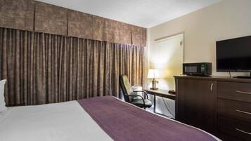 A hotel room with a large bed, a desk with a lamp, a television, and a wardrobe.