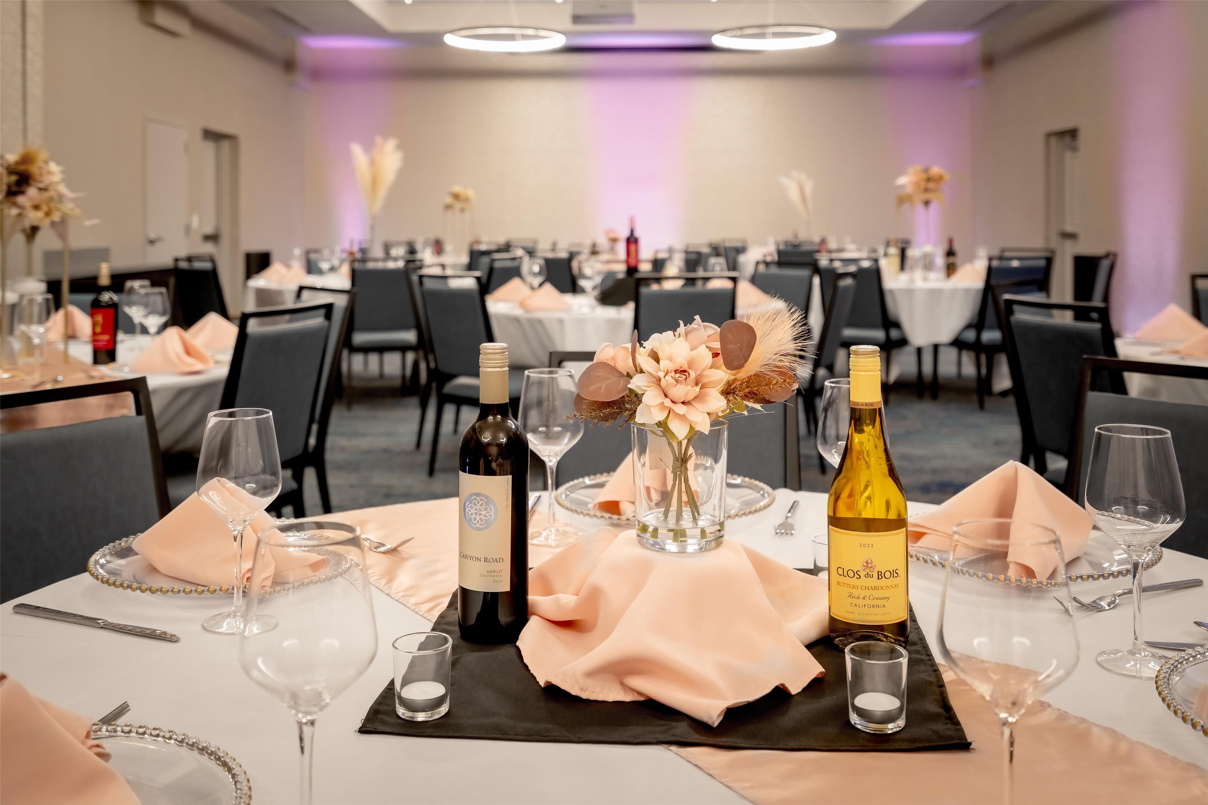 A banquet hall with tables set for a formal event, featuring wine bottles and floral centerpieces.