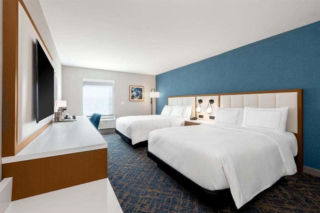 A hotel room with two beds, a desk, a TV, and a window.