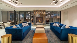 Un salon moderne avec deux canapés bleus, une cheminée centrale et un tapis à motifs.