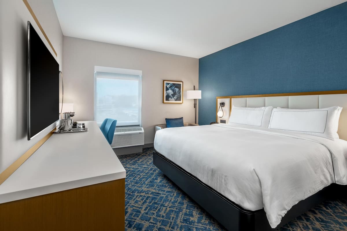 Habitación de hotel con una cama grande, un escritorio, un televisor de pantalla plana, una ventana con vistas y una pared de acento azul.