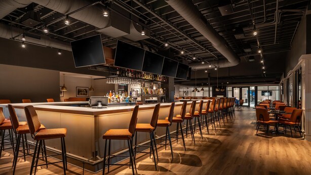 Un espace bar moderne doté d’un long comptoir, de nombreux tabourets et d’une grande variété de bouteilles et de verres.