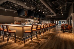 Una zona de bar moderna con una barra alargada, varios taburetes y una amplia variedad de botellas y vasos.