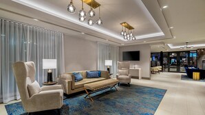 Un hall d’hôtel moderne avec un ensemble de canapés, des fauteuils, un tapis à motifs et des luminaires suspendus.