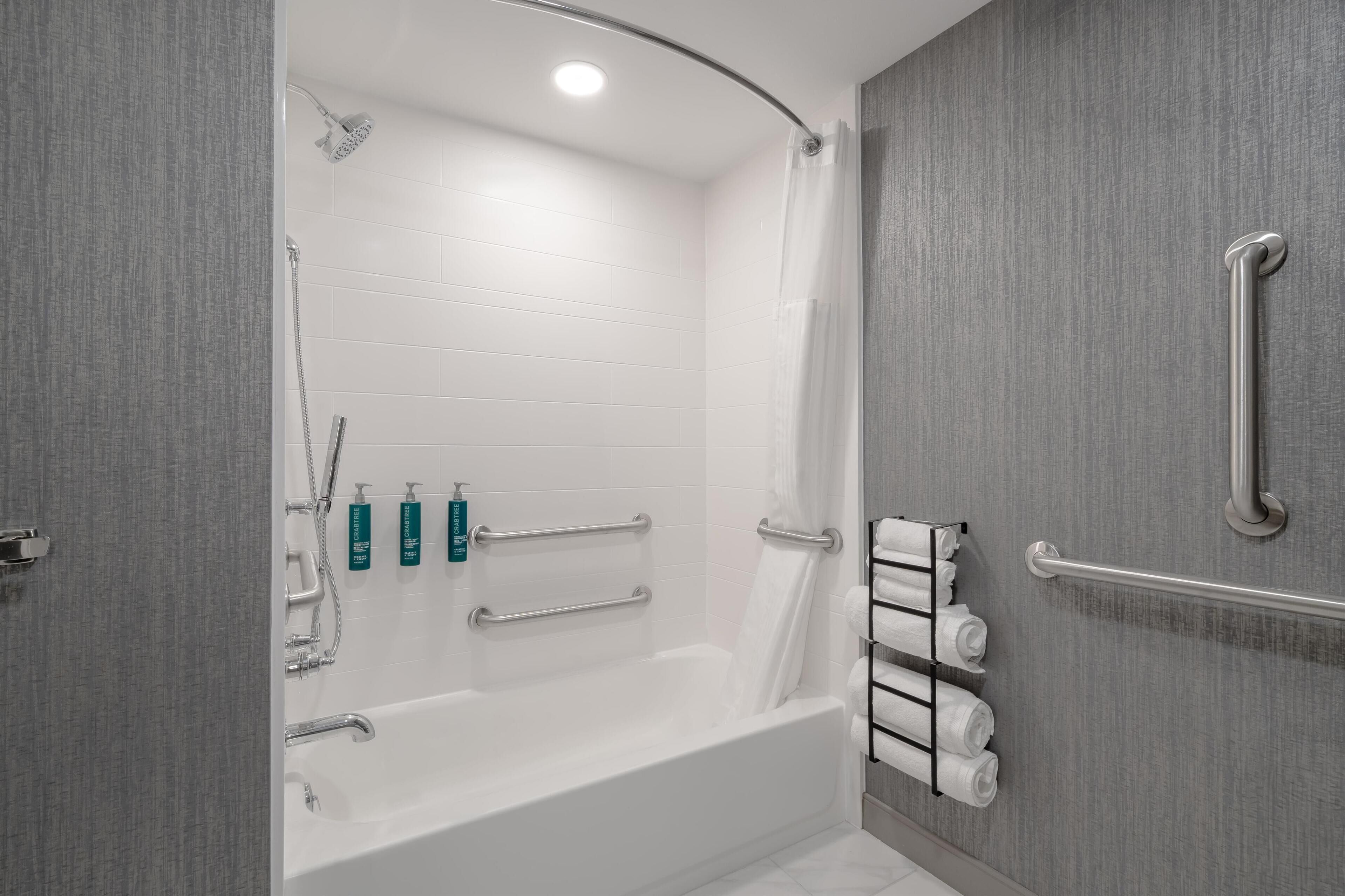 A modern bathroom with a bathtub, grab bars, and a towel rack.