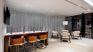 Un espace bar moderne avec un comptoir en bois, trois tabourets de bar et un téléviseur à écran plat fixé au mur.