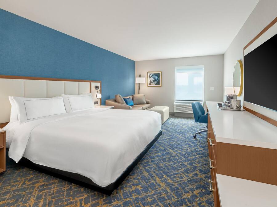 Une chambre d’hôtel avec un grand lit, un canapé, un bureau avec un téléviseur à écran plat et une grande fenêtre.