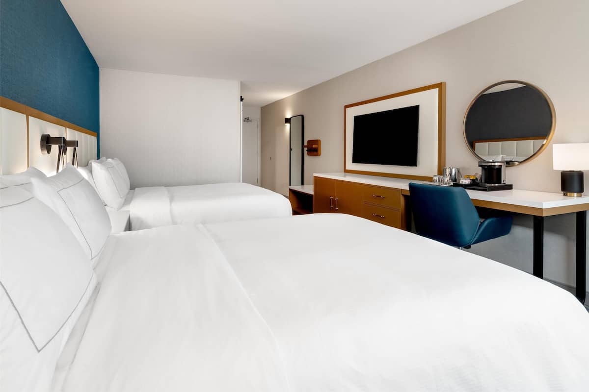 Habitación de hotel con dos camas, un escritorio, una silla, un espejo y un televisor.