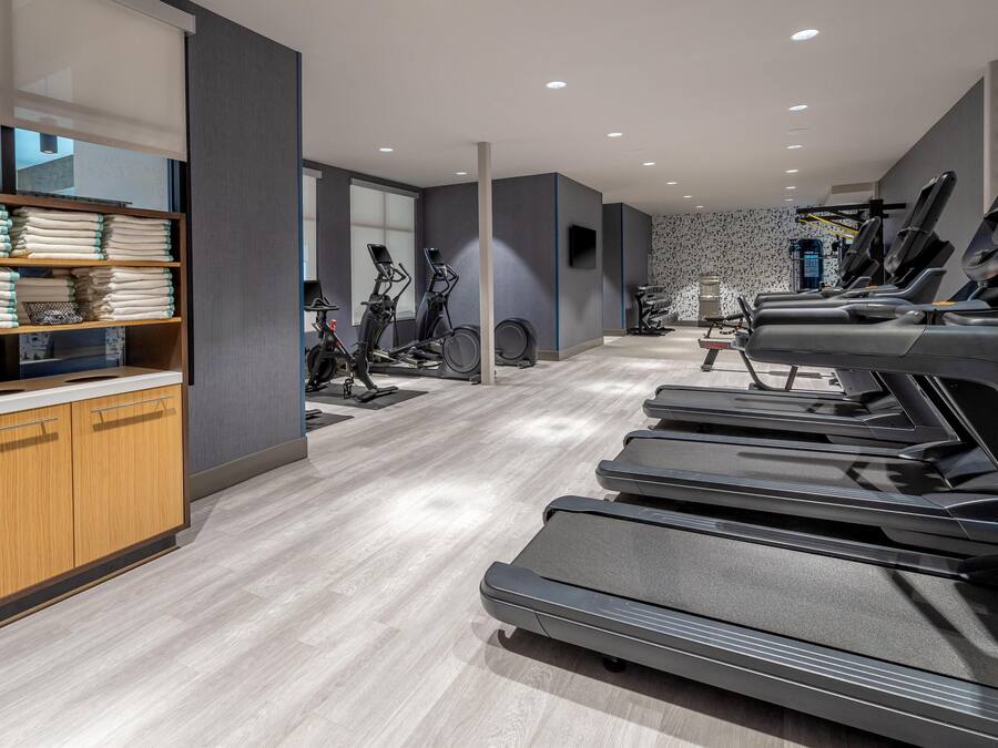 A modern gym with treadmills, stationary bikes, and a wooden cabinet with folded towels.