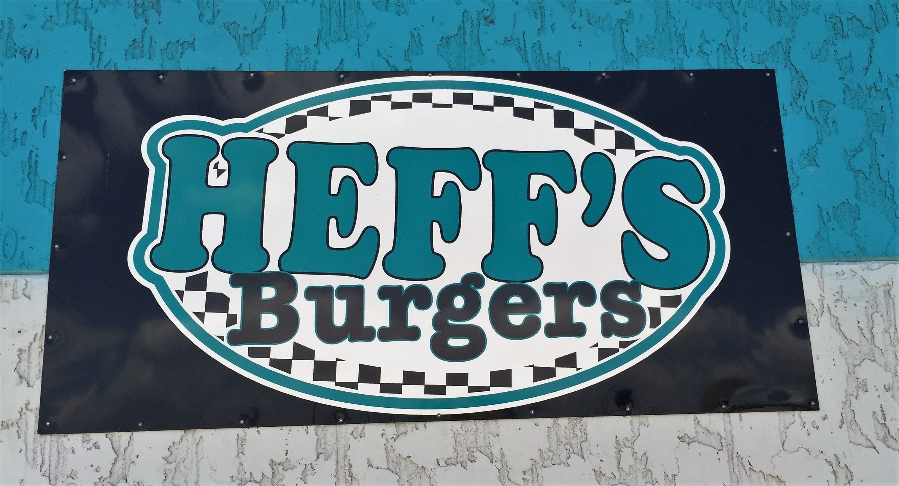 A sign for Heff's Burgers with a checkered pattern and teal and black colors.
