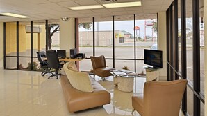 A spacious lobby with a large window, a comfortable seating area with sofas and chairs, a small coffee table, and a television on a stand. - Inn of the Conchos (San Angelo)