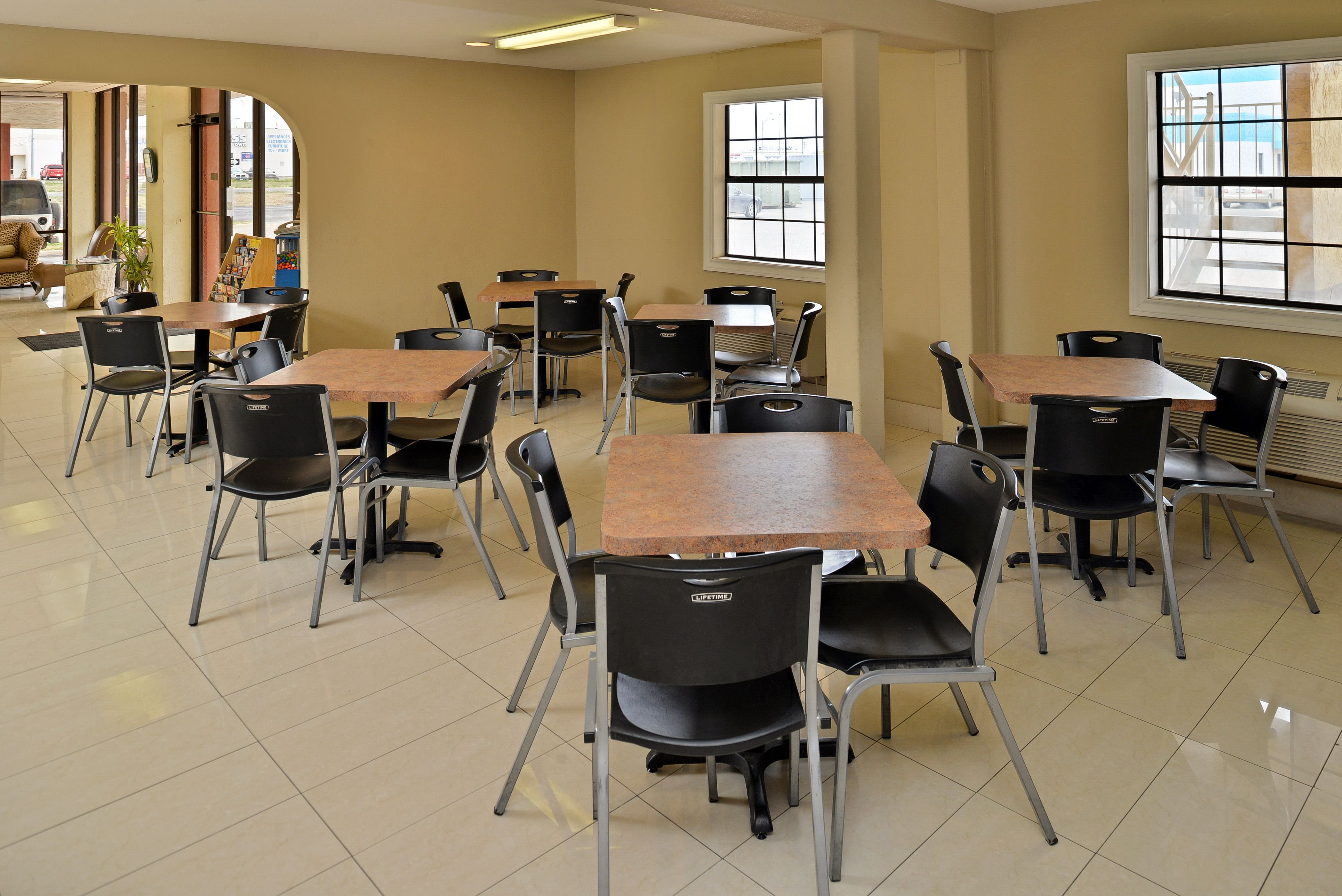 A classroom with multiple tables and chairs, large windows, and a view of the outside.