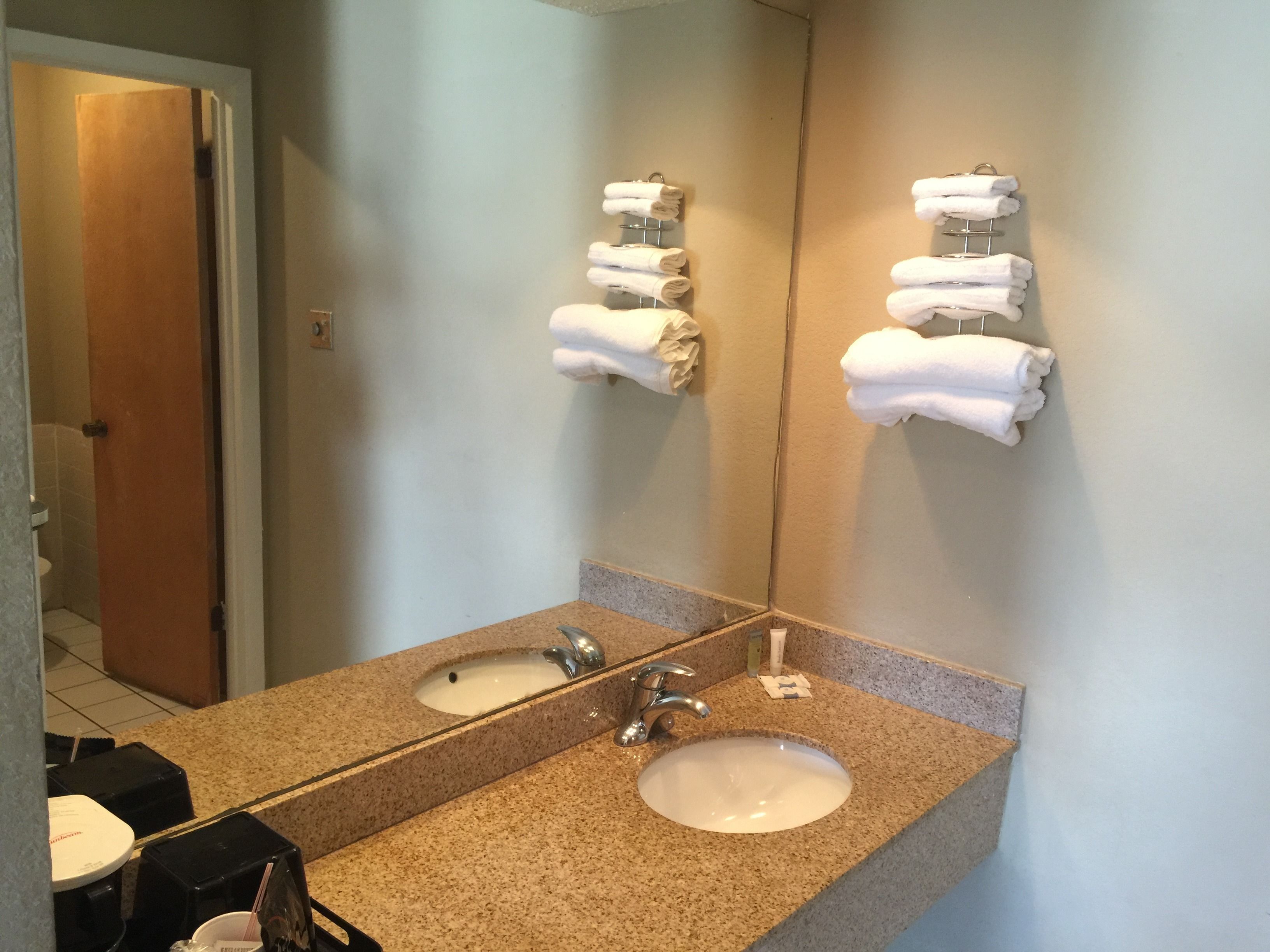 A bathroom with a granite countertop, a sink, and a mirror. There are two towel racks with towels on them.