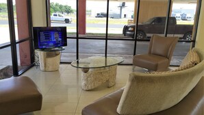 A hotel lobby with a glass coffee table, leather sofas, and a digital display. - Inn of the Conchos (San Angelo)