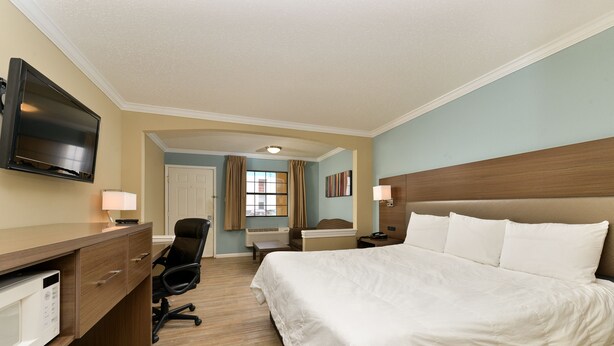 A hotel room with a bed, desk, chair, TV, and a window with curtains. - Inn of the Conchos (San Angelo)