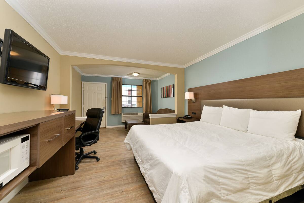 A hotel room with a bed, desk, chair, TV, and a window with curtains.