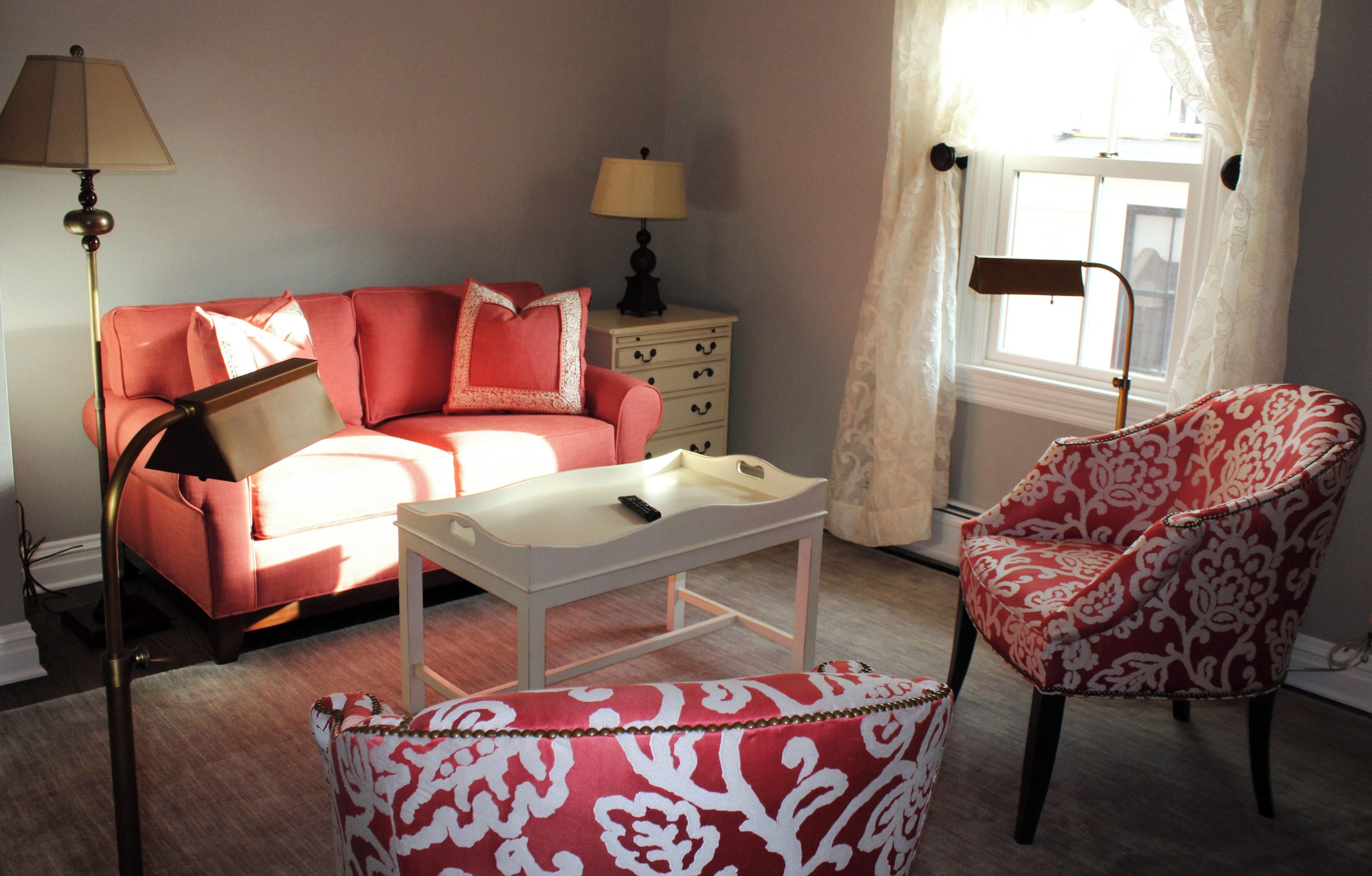 A room with a red sofa, a white side table, a patterned armchair, and two lamps.