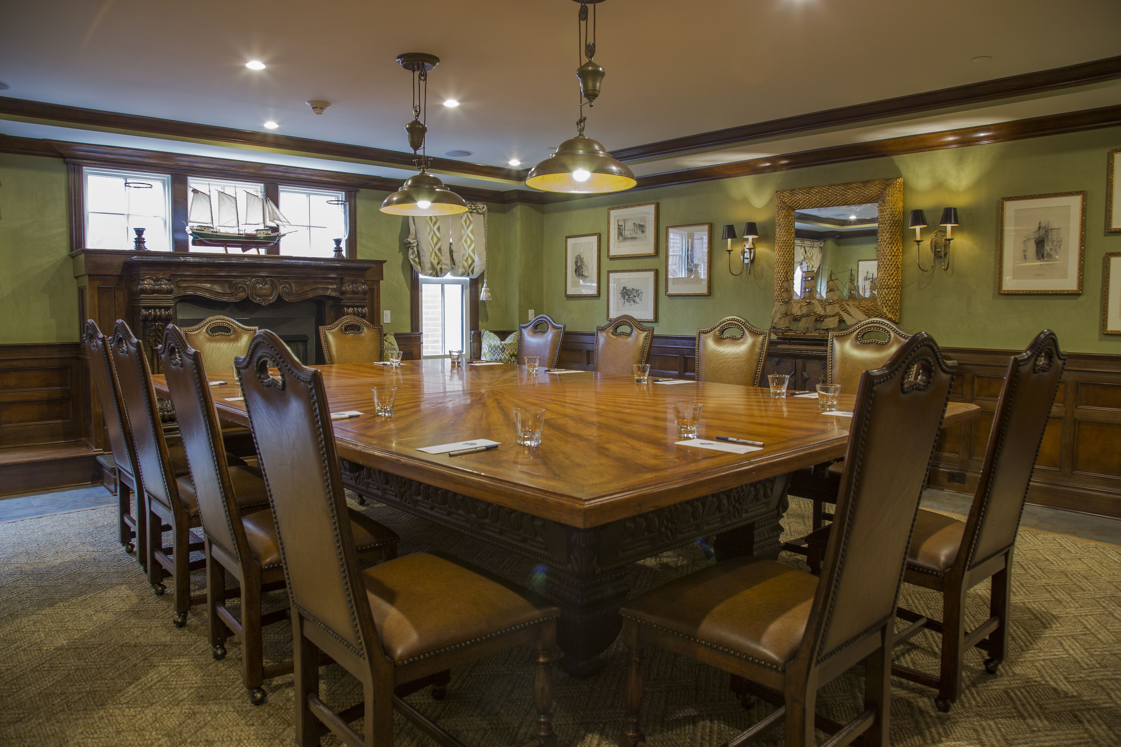 A conference room with a large wooden table, upholstered chairs, and pendant lighting.