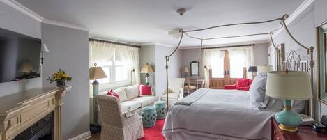 A hotel room with a four-poster bed, a fireplace, a sofa, and a dining area.
