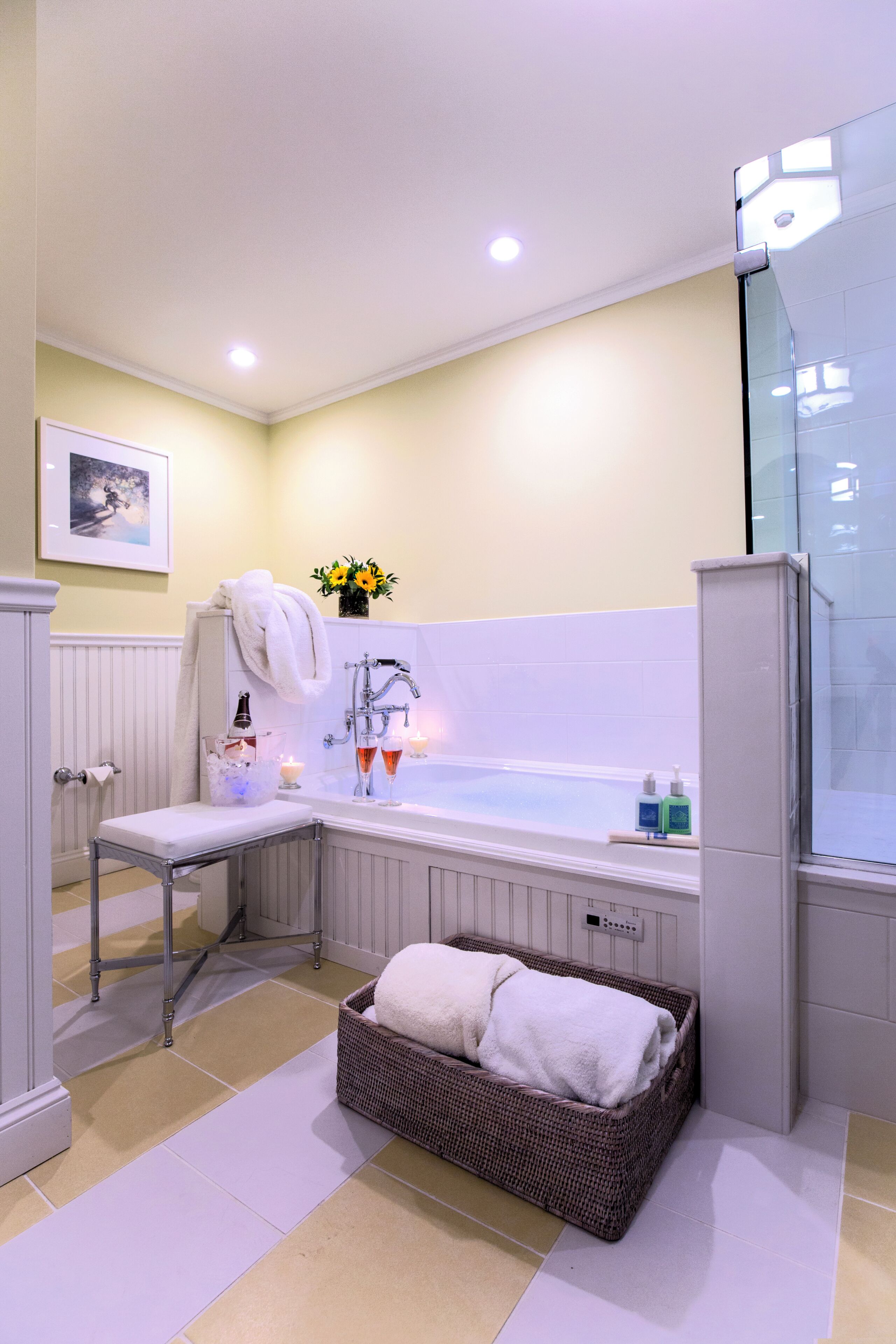A bathroom with a bathtub, a towel rack, a basket with towels, and a framed picture on the wall.
