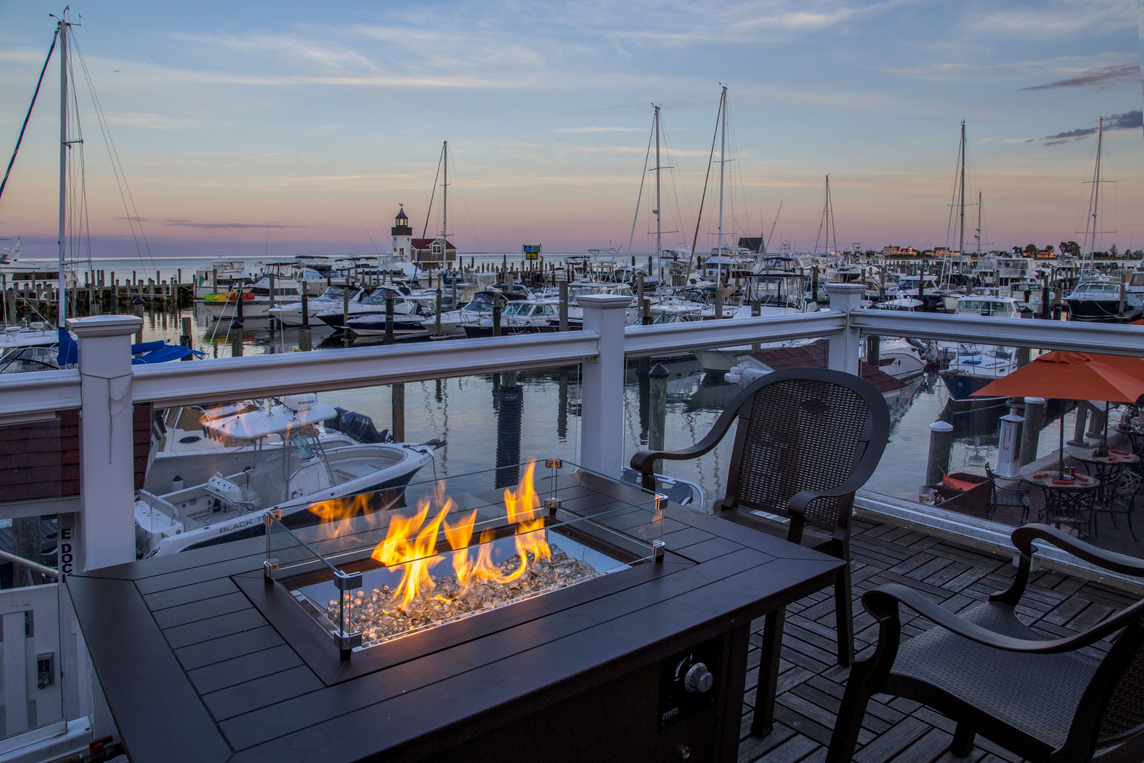 Un port de plaisance avec des bateaux amarrés, une table avec foyer intégré et des sièges d’extérieur.