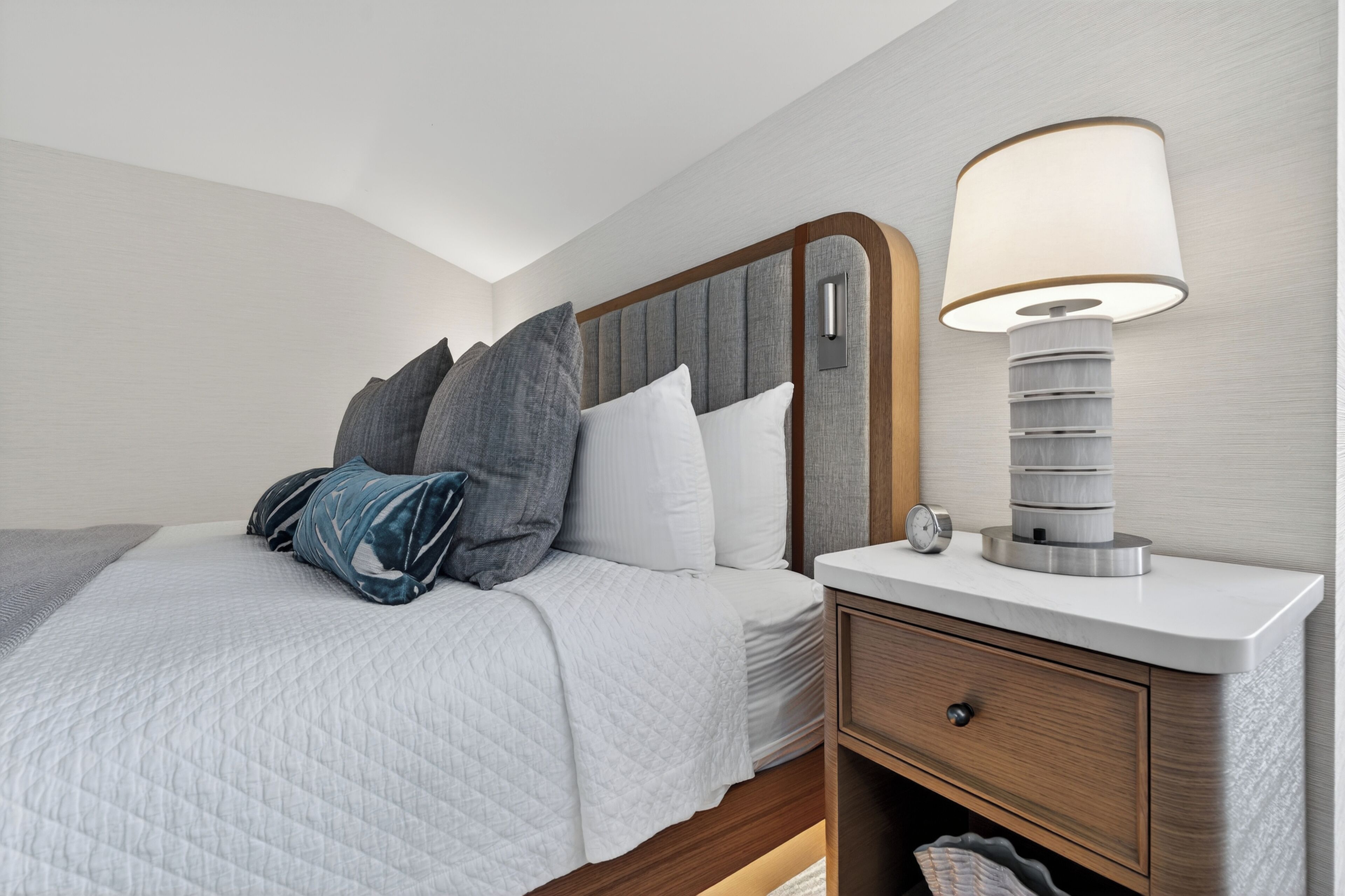 A neatly made bed with pillows, a bedside lamp, and a wooden nightstand with a drawer.
