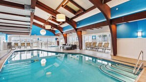 Une piscine intérieure à l’eau d’un bleu cristallin, avec des poutres en bois et des chaises longues.