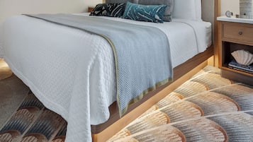Una cama bien hecha con cabecera, una mesita de noche con lámpara y un tapete estampado en el suelo.