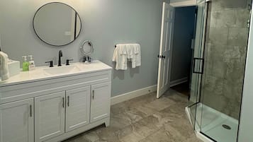A bathroom with a white vanity, a round mirror, a glass shower enclosure, and a towel rack.