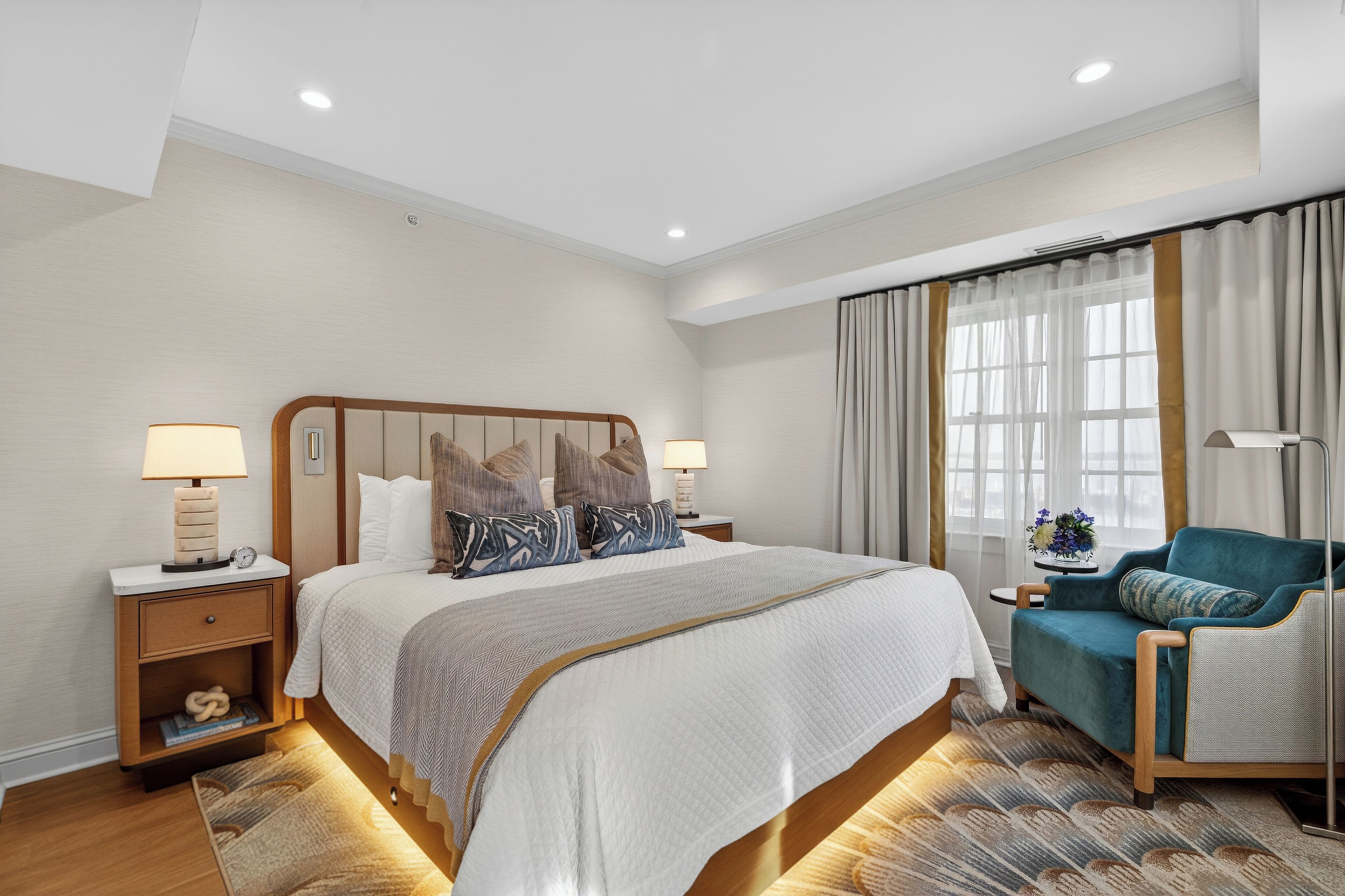 A hotel room with a large bed, bedside tables, a chair, a nightstand, a lamp, and a window with curtains.
