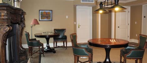A dining area with a round table, chairs, a chessboard, and a painting on the wall.