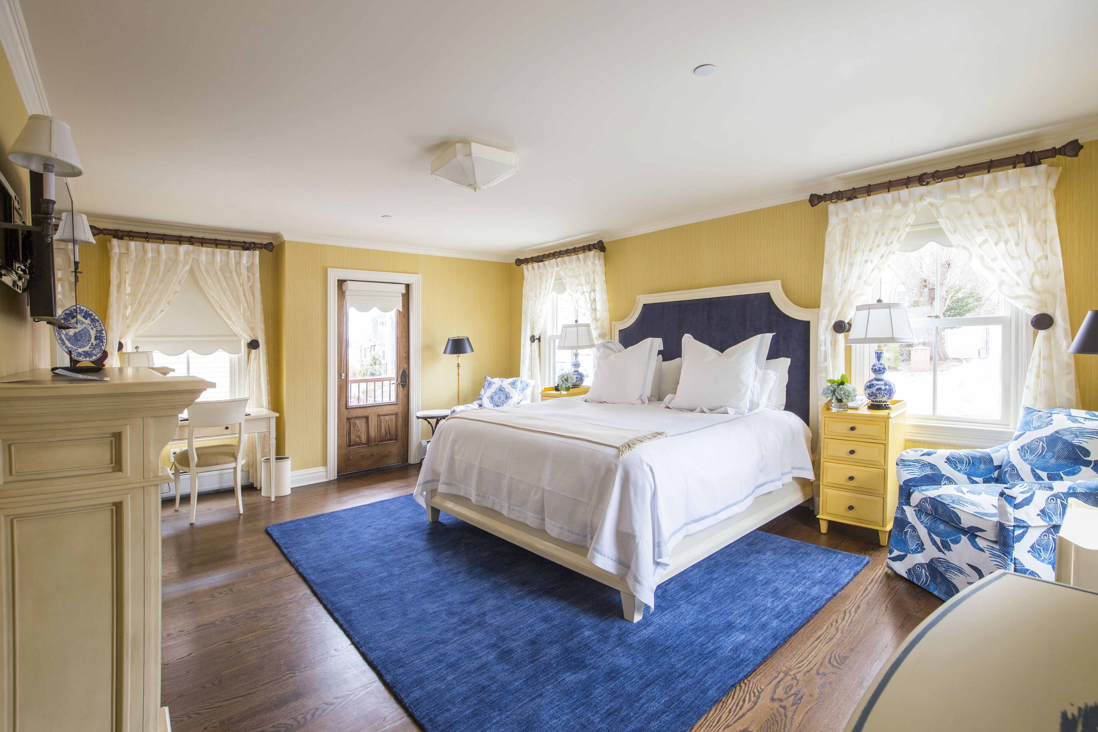 Un dormitorio con cama, mesitas de noche, cómoda, silla y ventana con cortinas.