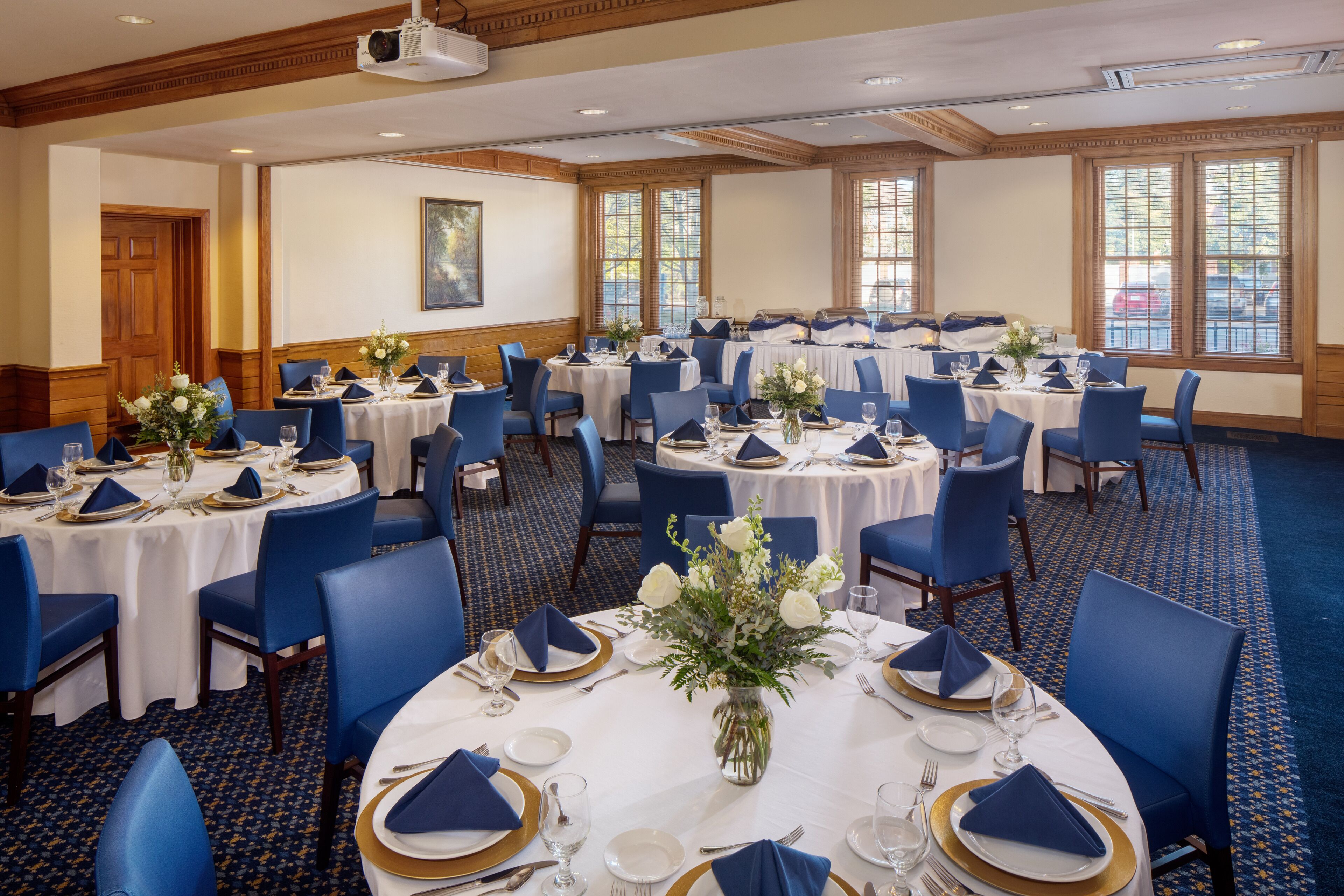 A banquet hall with round tables set for dining, featuring blue chairs and white tablecloths.