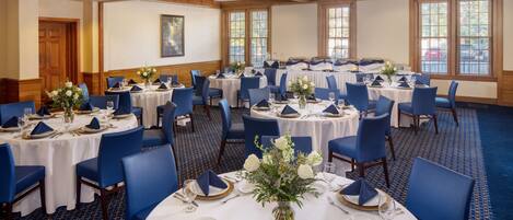 A banquet hall with round tables set for dining, featuring blue chairs and white tablecloths.