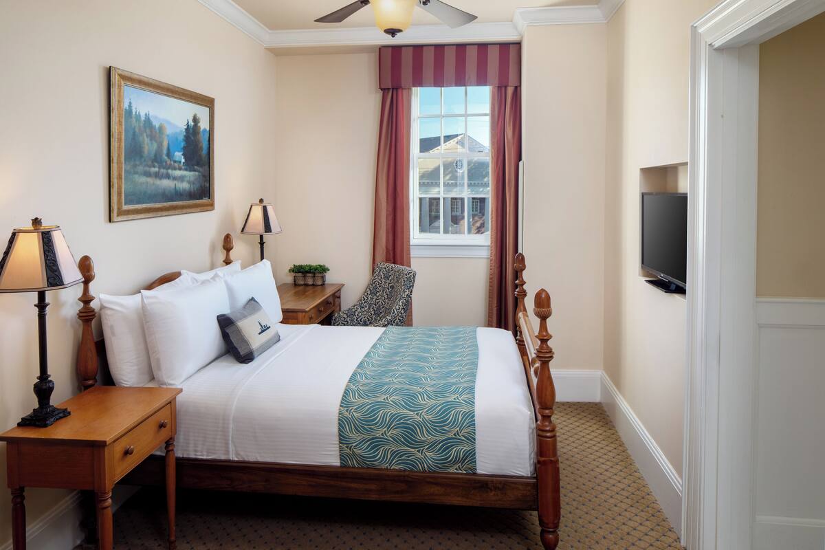 A neatly arranged bedroom with a bed, bedside table, lamp, and a painting on the wall.