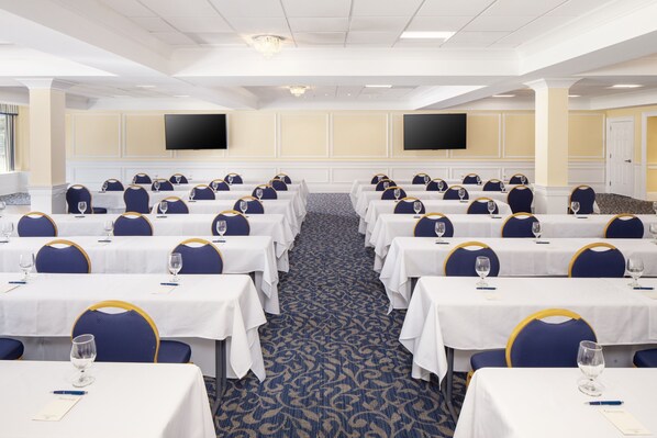 Un salón de conferencias con filas de mesas, sillas y un televisor de pantalla plana en la pared.