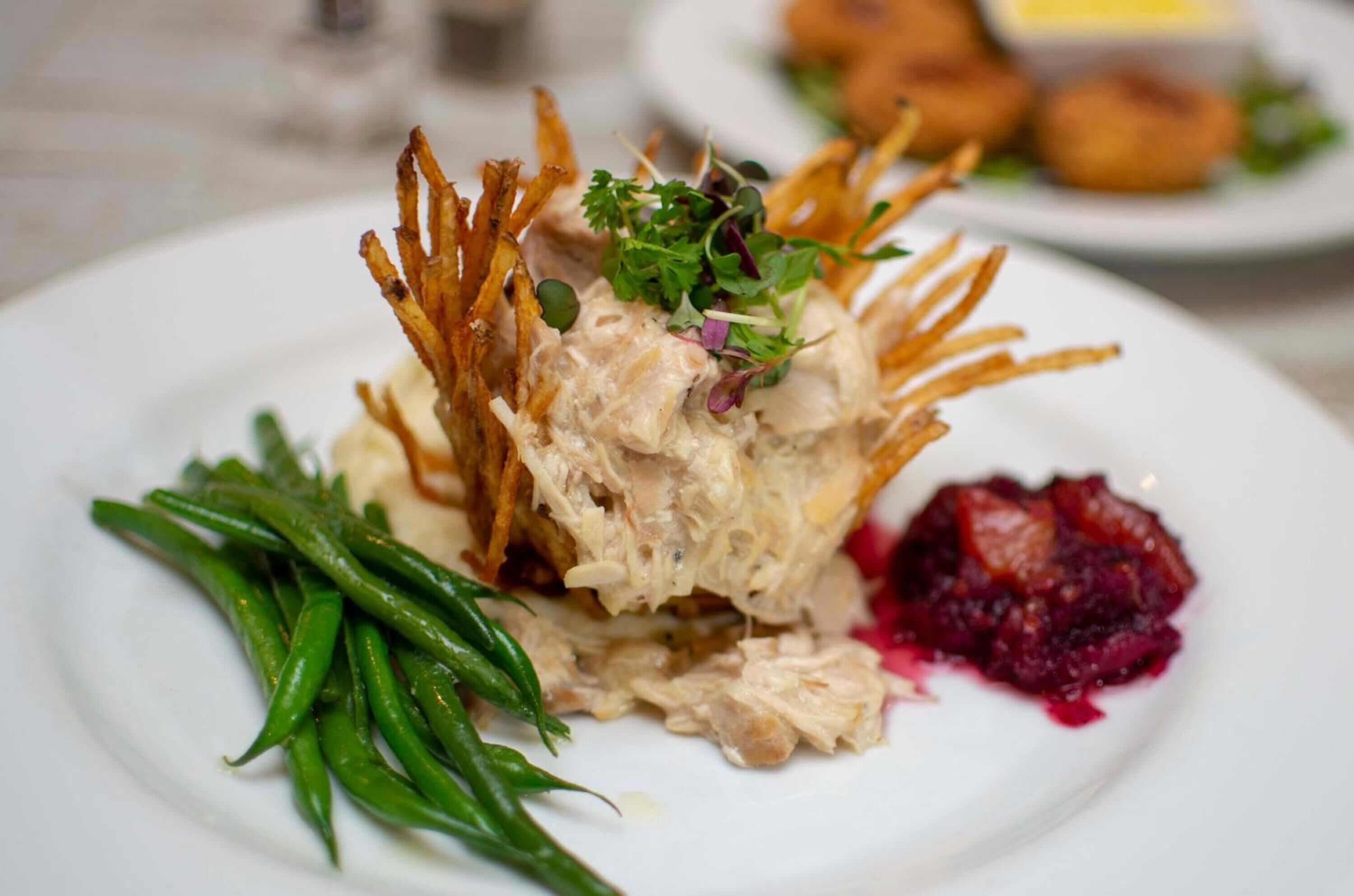 A plate with a dish of shredded chicken, green beans, and a side of red sauce.
