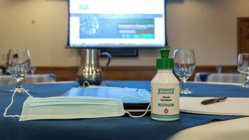 A hotel room with a table set for a meeting, a face mask, and a bottle of hand sanitizer.