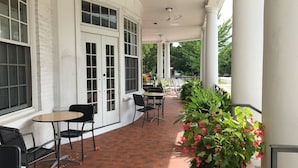 Un patio cubierto con suelo de ladrillo, columnas blancas y sillas de mimbre negro.